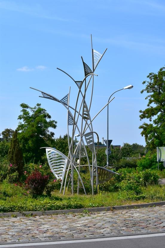 Foto der Skulptur umgeben von grünen Pflanzen in einem Kreisverkehr