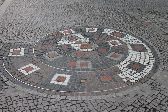 Foto des Fußweges mit dem Bodenmosaik in den Farben weiß, grau und ziegelrot.