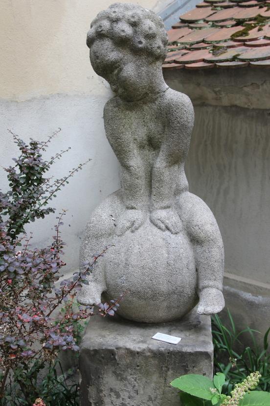 Skulptur eines kleinen Jungen auf einer Kugel sitzend.