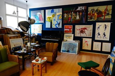 Foto eines Ateliers, mit einer dunkelgrauen Wand, die vollgehängt mit Kunstwerken ist.